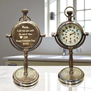 Könnte beinhalten: Eine Tischuhr aus Messing im Vintage-Stil mit rundem Zifferblatt und Ständer. Die Uhr hat ein weißes Zifferblatt mit schwarzen Ziffern und Zeigern. Die andere Seite der Uhr trägt eine eingravierte Botschaft: "Macey, ich werde dich bis ans Ende der Zeit lieben."