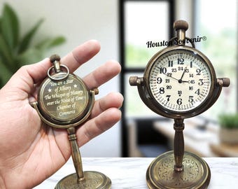 May include: Two antique brass desk clocks. One is a round clock with a white face and black numbers. The other is a compass-style clock with the text "You are a Star of Albany". Both clocks have decorative bases.