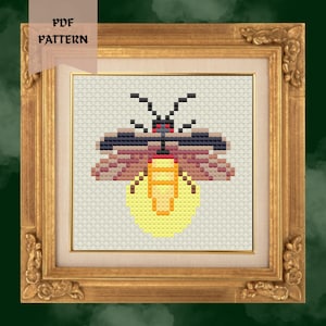 May include: Cross-stitch pattern of a firefly in a gold ornate frame. The firefly is pixelated with black, pink, and yellow colors. The text "PDF PATTERN" is in the upper left corner. The frame is rectangular with a gold finish.