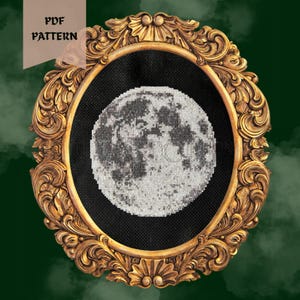 Pode incluir: Um ponto de cruz da lua, exibido em uma moldura dourada ornamentada. A lua é renderizada em tons de cinza e branco contra um fundo preto. As palavras "PDF PATTERN" estão no canto superior esquerdo.