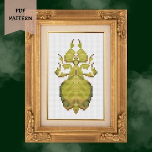 May include: A framed cross-stitch pattern featuring a green insect design. The insect is centered on a white background, framed by a gold-colored ornate frame. The words "PDF PATTERN" are in a banner in the upper left corner.