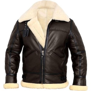 Puede incluir: Chaqueta de cuero marrón con forro y cuello de borrego color crema. La chaqueta tiene cremallera, dos bolsillos delanteros y ribetes negros. Los puños y el dobladillo también están forrados con borrego color crema.