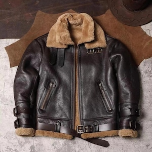 Puede incluir: Chaqueta bomber de cuero marrón oscuro con cuello y forro de borrego beige. La chaqueta tiene cremallera frontal, dos bolsillos con cremallera y correas ajustables en las mangas y la cintura. Tiene un estilo aviador clásico.