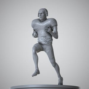 May include: A gray sculpture of a football player in a running pose, holding a football. The figure wears a helmet and uniform with the number 5. The sculpture is on a round base.