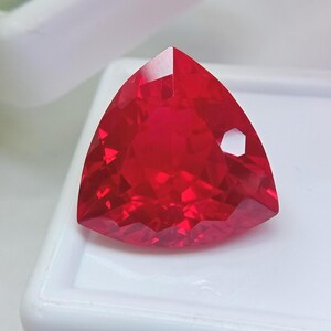 Peut inclure: Une pierre précieuse rouge vif et transparente taillée en forme triangulaire avec de multiples facettes. La pierre présente une surface brillante et réfléchissante avec des bords nets et une teinte cramoisie profonde, révélant une structure géométrique claire.