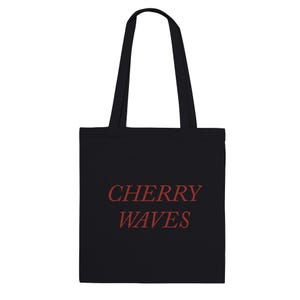 May include: Black tote bag with the words "CHERRY WAVES" in red script. The bag has two black handles and is made of a solid black material. The text is centered on the front of the bag.