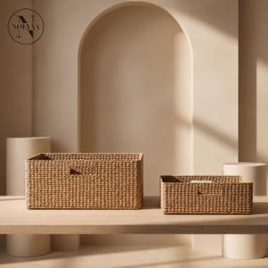 Puede incluir: Dos cestas de almacenamiento rectangulares hechas de fibras naturales trenzadas de color tostado. Cada cesta presenta una textura trenzada uniforme y apretada, con asas rectangulares recortadas en la parte frontal.
