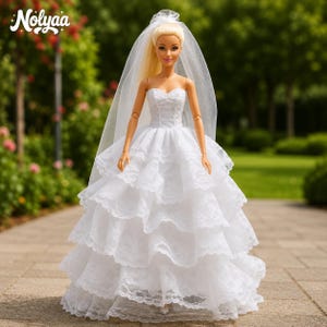 Può includere: Bambola bionda con un abito da sposa bianco senza spalline con più strati a balze. La bambola ha un velo trasparente ed è in piedi su una superficie pavimentata con uno sfondo verde sfocato. Il marchio "Nolyaa" è visibile.