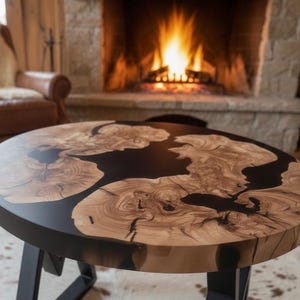 Puede incluir: Una mesa de centro redonda de madera con incrustaciones de resina negra. La mesa tiene un patrón de vetas de madera natural y se apoya sobre una base de metal negro. La mesa tiene unos 91 cm de diámetro.