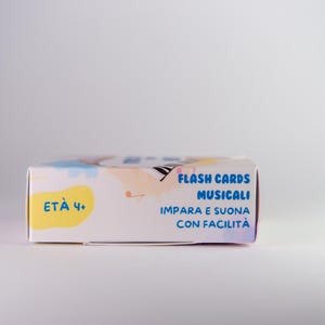 K&ouml;nnte beinhalten: Eine rechteckige, wei&szlig;e Schachtel mit musikalischen Lernkarten. Sie zeigt farbenfrohe Illustrationen und italienischen Text, darunter "FLASH CARDS MUSICALI" und "ET&Agrave; 4+".