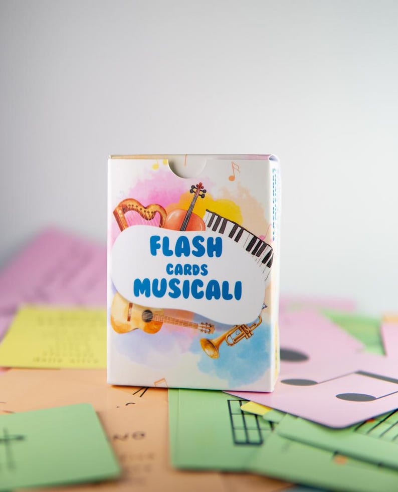 K&ouml;nnte beinhalten: Eine Schachtel mit musikalischen Lernkarten mit Abbildungen einer Harfe, einer Geige, Klaviertasten, einer Gitarre und einer Trompete. Auf der Schachtel steht "FLASH CARDS MUSICALI" in Blau. Bunte Lernkarten mit Noten liegen verstreut.