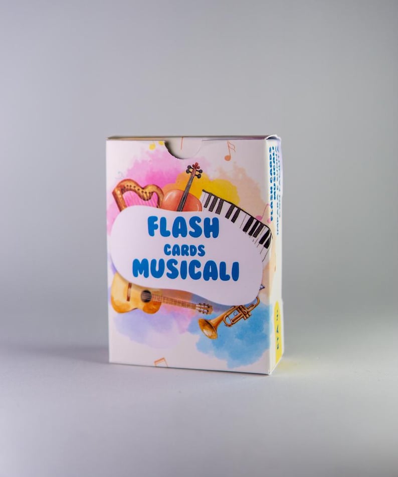 K&ouml;nnte beinhalten: Eine wei&szlig;e Schachtel mit Lernkarten mit den Worten "FLASH CARDS MUSICALI" in Blau. Die Schachtel zeigt Illustrationen von Musikinstrumenten wie Harfe, Geige, Klaviertasten, Gitarre und Trompete, vor einem farbenfrohen Aquarellhintergrund.