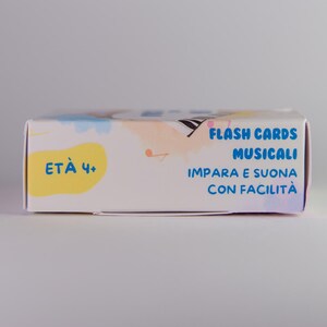 K&ouml;nnte beinhalten: Eine wei&szlig;e rechteckige Schachtel mit Lernkarten mit dem Text "FLASH CARDS MUSICALI" in Blau. Die Schachtel hat auch den Text "ET&Agrave; 4+" in einem gelben Oval. Die Schachtel hat ein farbenfrohes Design mit Pastellfarben.