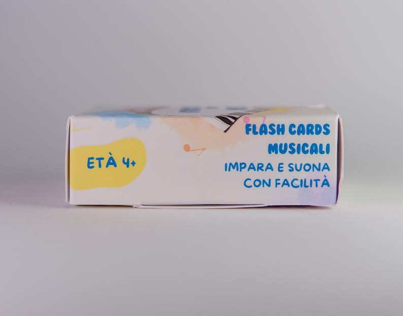 K&ouml;nnte beinhalten: Eine wei&szlig;e rechteckige Schachtel mit Lernkarten mit dem Text "FLASH CARDS MUSICALI" in Blau. Die Schachtel hat auch den Text "ET&Agrave; 4+" in einem gelben Oval. Die Schachtel hat ein farbenfrohes Design mit Pastellfarben.