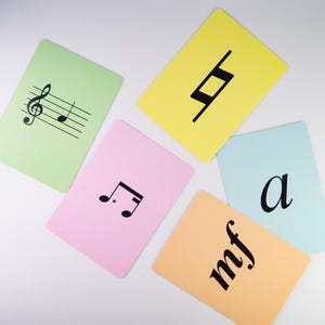 K&ouml;nnte beinhalten: Eine Sammlung farbiger Karteikarten mit musikalischen Symbolen und Begriffen. Die Karten sind in verschiedenen Pastellfarben gehalten, darunter Gr&uuml;n, Rosa, Gelb, Orange und Blau. Jede Karte zeigt ein anderes musikalisches Symbol oder einen Begriff in Schwarz, wie einen Violinschl&uuml;ssel, eine Viertelpause und die Buchstaben "mf".