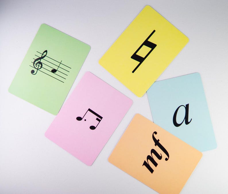 K&ouml;nnte beinhalten: Eine Sammlung farbiger Karteikarten mit musikalischen Symbolen und Begriffen. Die Karten sind in verschiedenen Pastellfarben gehalten, darunter Gr&uuml;n, Rosa, Gelb, Orange und Blau. Jede Karte zeigt ein anderes musikalisches Symbol oder einen Begriff in Schwarz, wie einen Violinschl&uuml;ssel, eine Viertelpause und die Buchstaben "mf".