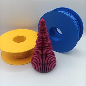 May include: A magenta 3D-printed tree with a ribbed, tiered structure standing in front of a yellow plastic filament spool on the left and a blue plastic filament spool on the right. The tree has a pointed top and a rounded, wide base.