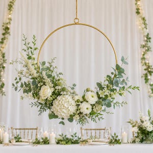 May include: A gold metal hoop suspended by a thin cord, adorned with a floral arrangement featuring white roses, hydrangeas, and ranunculus flowers, accented with green eucalyptus leaves and various small white filler blossoms and greenery.