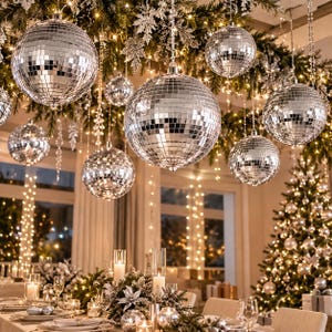 May include: Multiple silver mirrored disco balls of varying sizes hang from a ceiling decorated with evergreen branches and warm string lights, positioned above a dining table set with candles and silver ornaments in a room.