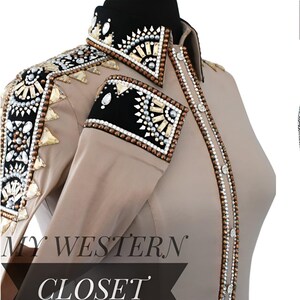May include: Tan western shirt with elaborate embellishments. The shirt features a black collar and cuffs, adorned with sparkling crystals and decorative elements. The front of the shirt is embellished with a line of small, round, white buttons. The text "MY WESTERN CLOSET" is visible.