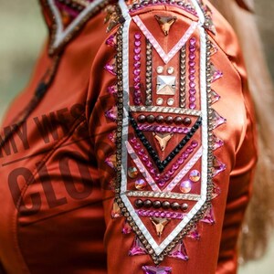 Könnte beinhalten: Rostfarbenes Satinhemd mit aufwendigen Verzierungen. Schulter und Ärmel weisen ein geometrisches Design mit weißen, schwarzen und rosa Akzenten sowie klaren und rosa Kristallen auf. Der Text "MY WESTERN GLOW" ist teilweise sichtbar.
