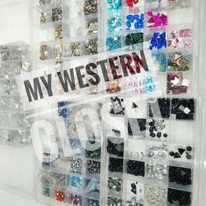 May include: Clear plastic organizer filled with various colorful rhinestones and gems. The compartments hold different shapes and sizes of crystals in shades of silver, gold, blue, pink, and black. Text on the image reads "MY WESTERN CLOS".
