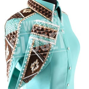 Peut inclure: Une chemise de spectacle Western turquoise avec des ornements complexes. La chemise présente des motifs géométriques marron et turquoise sur les épaules et les poignets, rehaussés de strass et de perles. Le col et les poignets sont également ornés d'éléments décoratifs.