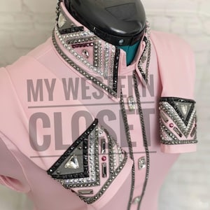 Könnte beinhalten: Ein hellrosa Western-Show-Shirt mit aufwendigen Strass- und Kristallverzierungen an Kragen, Manschetten und Vorderseite. Das Shirt hat ein klassisches Western-Design mit Knopfleiste und langen Ärmeln. Der Text "MY WESTERN CLOSET" ist auf der Vorderseite aufgedruckt.