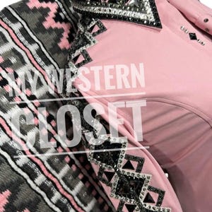 Puede incluir: Una camisa de exhibición occidental rosa claro con adornos de pedrería y gemas en el cuello y las mangas. La camisa se combina con una manta estampada gris, rosa y blanca. El texto "MY WESTERN CLOSET" es visible en la camisa.