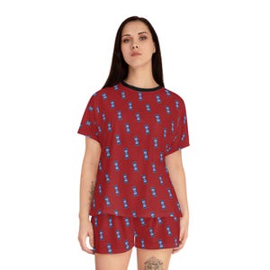 May include: Red pajama set with a repeating pattern of blue rectangles. The short-sleeved top has a black trim around the neckline and sleeves. The matching shorts complete the two-piece sleepwear set.