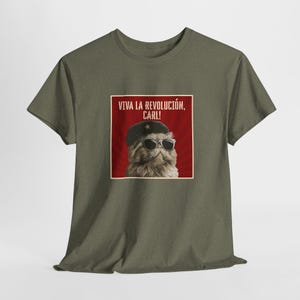 May include: An olive green t-shirt with a graphic of a cat wearing sunglasses and a beret. The graphic includes the text "VIVA LA REVOLUCIÓN, CARL!" in red and white. The cat is set against a red background.