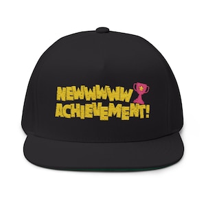 May include: A black baseball cap featuring embroidered yellow text that reads NEWWWWW ACHIEVEMENT! with a small pink trophy icon containing a yellow star. The cap has a structured crown and a flat brim, showcasing a clean and simple design.