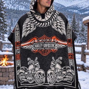 May include: A black hooded poncho featuring a white and orange Harley-Davidson logo, winged graphics, and two motorcycle illustrations. The garment includes vertical text reading Harley-Davidson along the sides and a fringe hem at the bottom.
