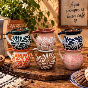 May include: A set of six small ceramic mugs with rounded bodies and handles, featuring hand-painted floral patterns in dark green, orange, pink, brown, and blue. The mugs are arranged in two stacks of three on a wooden surface with coffee beans.