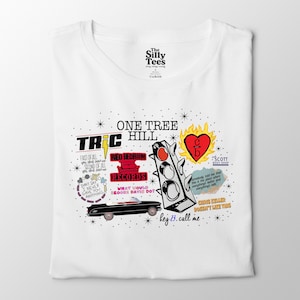 May include: White t-shirt featuring a colorful graphic design with the text "ONE TREE HILL". The design includes a traffic light, a red heart with "C/B", and other text elements. The shirt is folded.