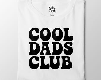 May include: A folded white t-shirt featuring the words "COOL DADS CLUB" in large, black, rounded letters. The brand label "The Silly Tees" is at the top. A simple, casual garment for everyday wear.
