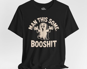 May include: Black t-shirt featuring a cartoon ghost graphic with the text "MAN THIS SOME BOOSHIT". The ghost has its arms outstretched. The text and graphic are in a distressed, vintage style. The t-shirt is a crew neck style.