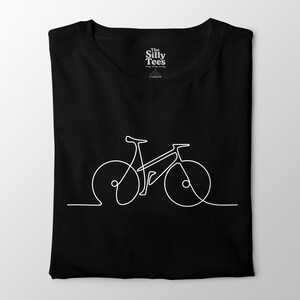 Puede incluir: Camiseta negra con un dibujo lineal blanco de una bicicleta. La camiseta tiene cuello redondo y mangas cortas. El texto "The Silly Tees" está impreso en la parte superior de la espalda de la camiseta.