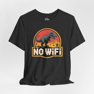 May include: Dark grey t-shirt with a cartoon dinosaur design inside a red and yellow circle, and the text "NO WIFI". The design includes desert scenery with cacti and mountains.