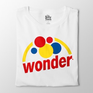 May include: White t-shirt featuring a colorful graphic design. The design includes a yellow semi-circle, red, yellow, and blue circles, and the word "wonder" in red, angled across the bottom.