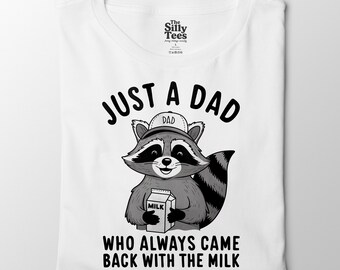 Pode incluir: Camiseta branca com um guaxinim de desenho animado segurando uma caixa de leite. O texto diz "JUST A DAD WHO ALWAYS CAME BACK WITH THE MILK". O guaxinim usa um chapéu que diz "DAD". A camisa tem uma etiqueta que diz "The Silly Tees".