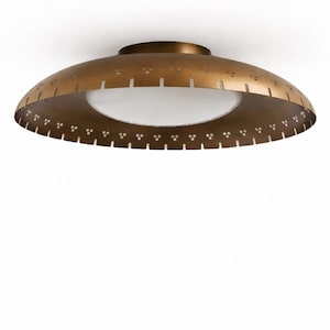 May include: A brass-coloured, mid-century modern ceiling light fixture. The fixture has a rounded, saucer-like shape with a white, circular light source in the centre. Decorative cutouts and perforations adorn the outer rim.