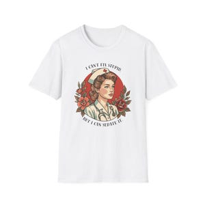 May include: A white short-sleeve t-shirt featuring a graphic of a nurse in a cap and uniform with a stethoscope. The design includes red roses and a red circle background with the text, I CAN'T FIX STUPID. BUT I CAN SEDATE IT.
