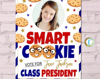 May include: A white and blue striped background with a red, white, and blue cookie design. The text "SMART COOKIE" is in red and blue letters. The text "VOTE FOR Jane Jackson CLASS PRESIDENT" is in gold letters. A photo of a girl is in a circle in the middle of the poster.