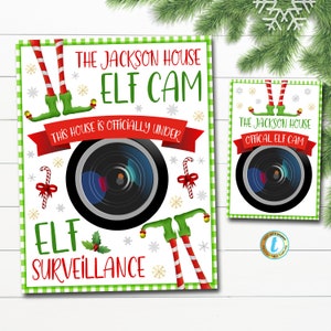 以下が含まれることがあります： 緑と白のチェック柄の背景を持つ印刷可能なサイン。サインには、エルフの足と「The Jackson House Elf Cam This house is officially under Elf Surveillance」というテキストが書かれたカメラレンズが描かれています。