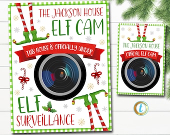 May include: A printable sign with a green and white checkered background. The sign features a camera lens with elf legs and the text "The Jackson House Elf Cam This house is officially under Elf Surveillance".