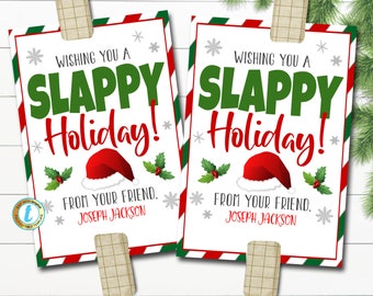 May include: Two holiday greeting cards with the text "Wishing You a Slappy Holiday!" in green and red. Each card features a Santa hat illustration, holly, and the name "Joseph Jackson". The cards are clipped to a white surface.