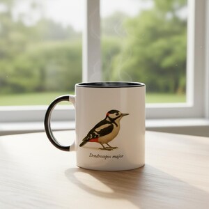 May include: A white ceramic mug with a black handle and rim, featuring a detailed illustration of a great spotted woodpecker with black, white, and red plumage. The text Dendrocopos major is printed in black below the bird illustration.