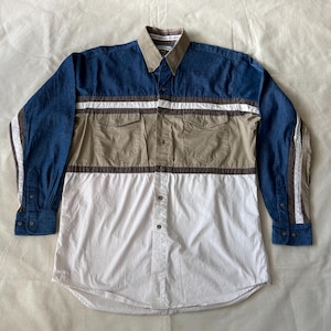 Puede incluir: Una camisa de manga larga con botones que presenta un diseño de bloques de color con una sección superior de mezclilla azul, un panel central color canela con dos bolsillos en el pecho y una sección inferior blanca. El cuello es canela.