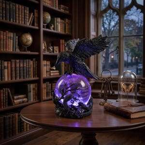 May include: A black raven sculpture perched on a glowing purple crystal ball, featuring a detailed tree branch design. The statue is on a dark wooden table in a library, with bookshelves and a window in the background.